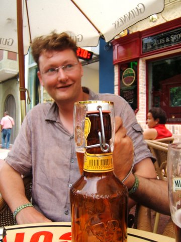 a man with glasses sitting in front of a bottle of beer