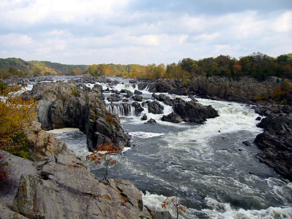 a river flows near some rocks and fall foliage