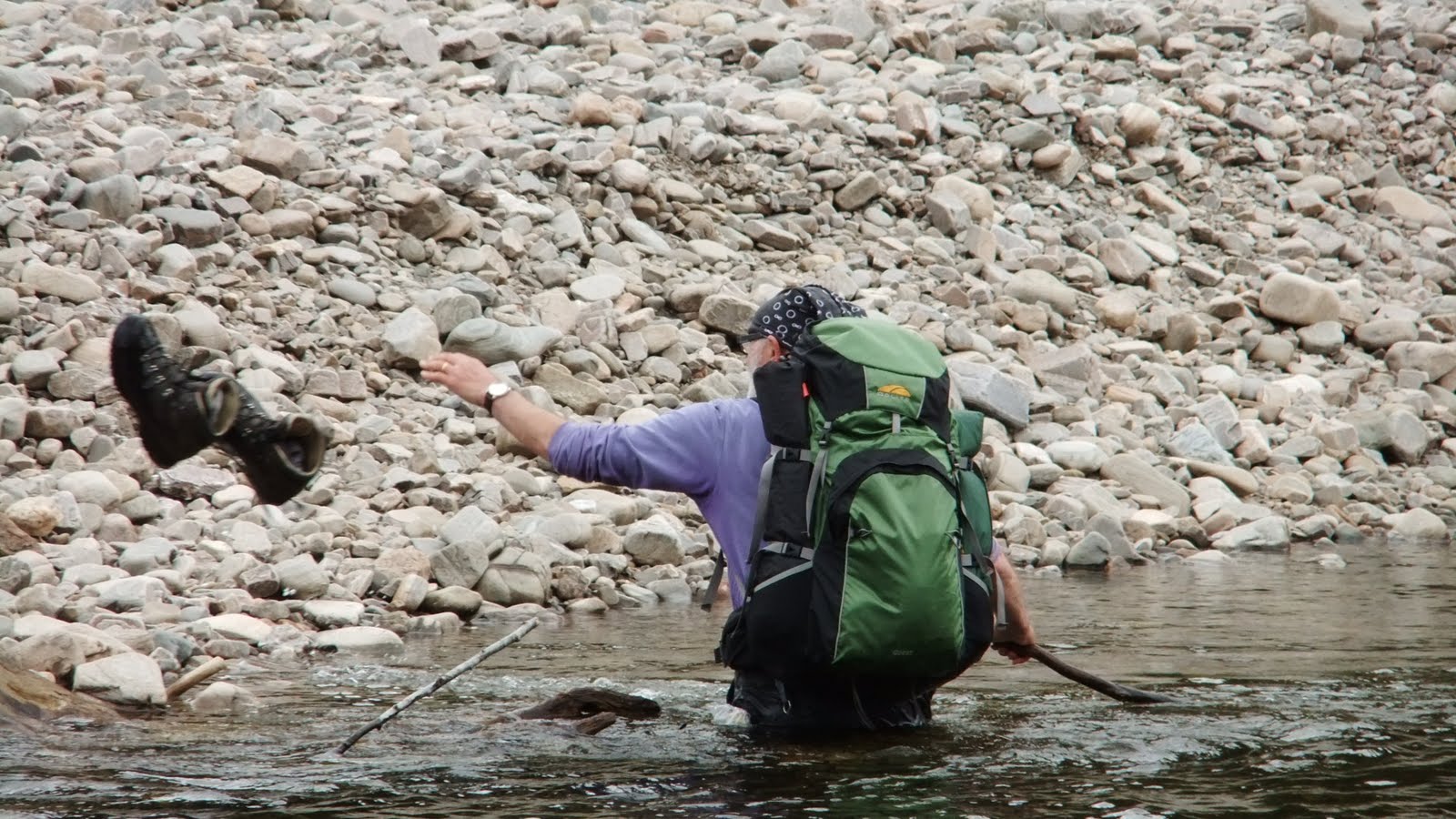 a man wades through a stream with a backpack on and a bird flying towards him