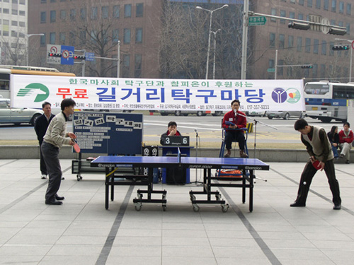 people playing ping pong on a city street