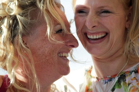 two women laughing close to each other while one looks at her cell phone