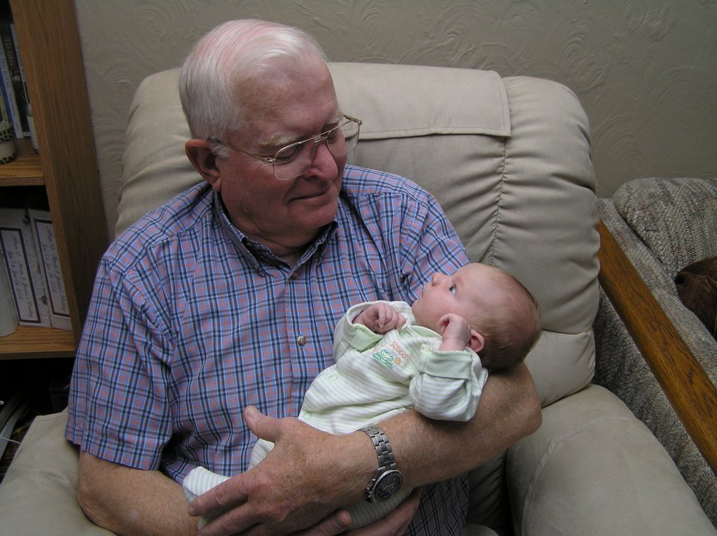 an older man holding a baby while sitting in a chair