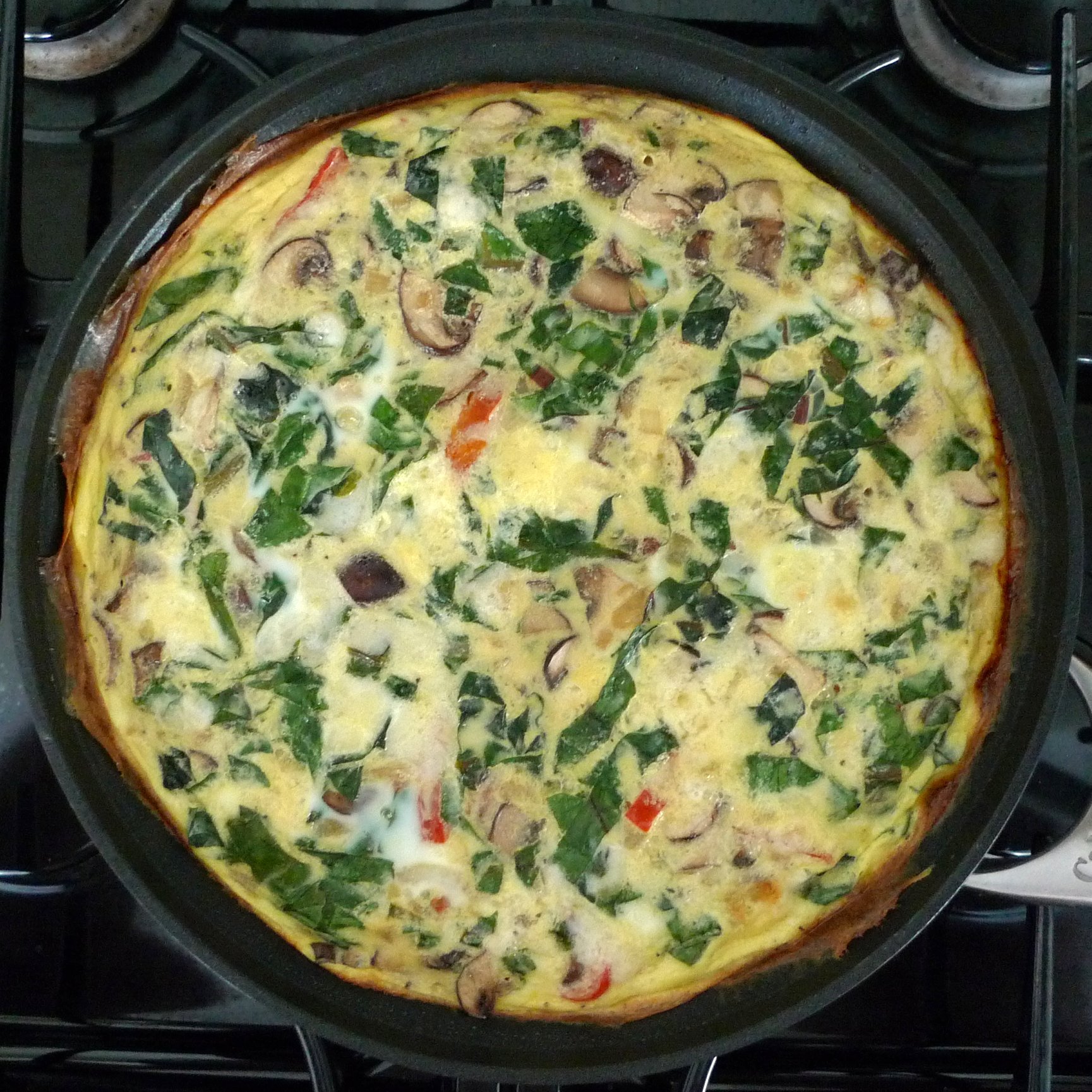 pizza with spinach leaves, mushrooms, and onions being cooked in the oven