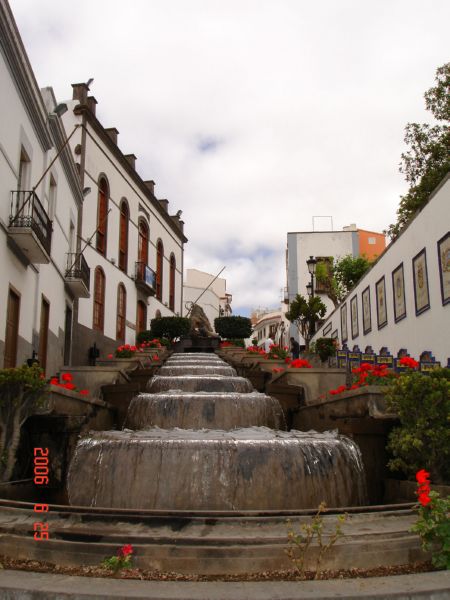 there are flowers surrounding the waterfall in the town square