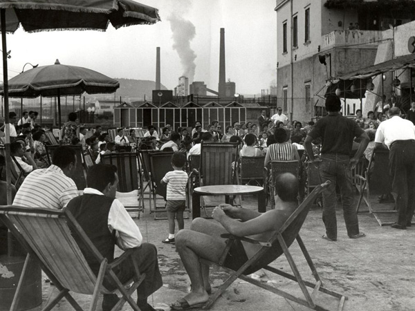 people sitting and standing in chairs outside a factory
