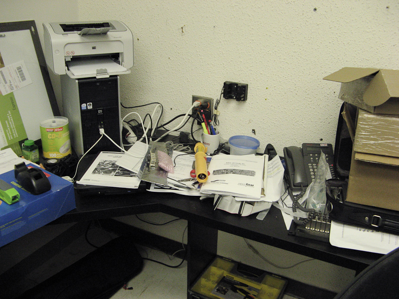 an office desk has electronics, equipment and papers on it