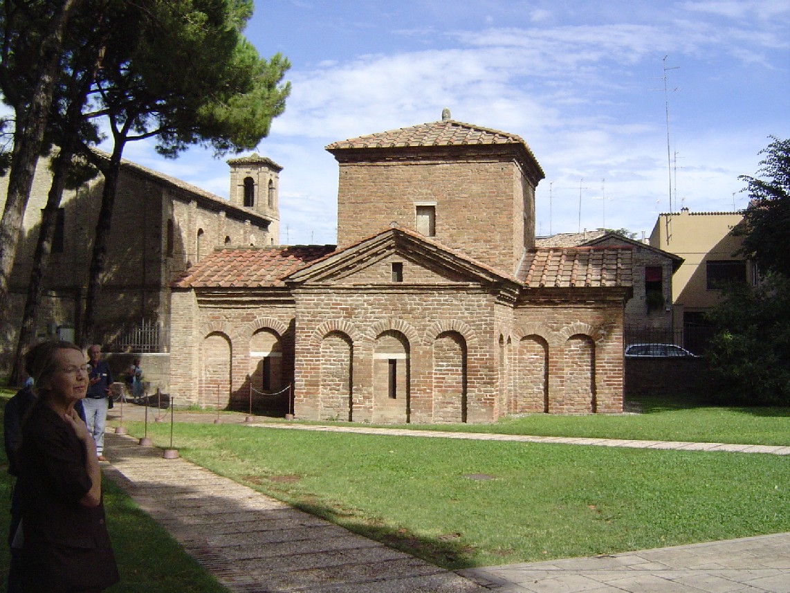 a brick building with three steeples sits near grass and a sidewalk