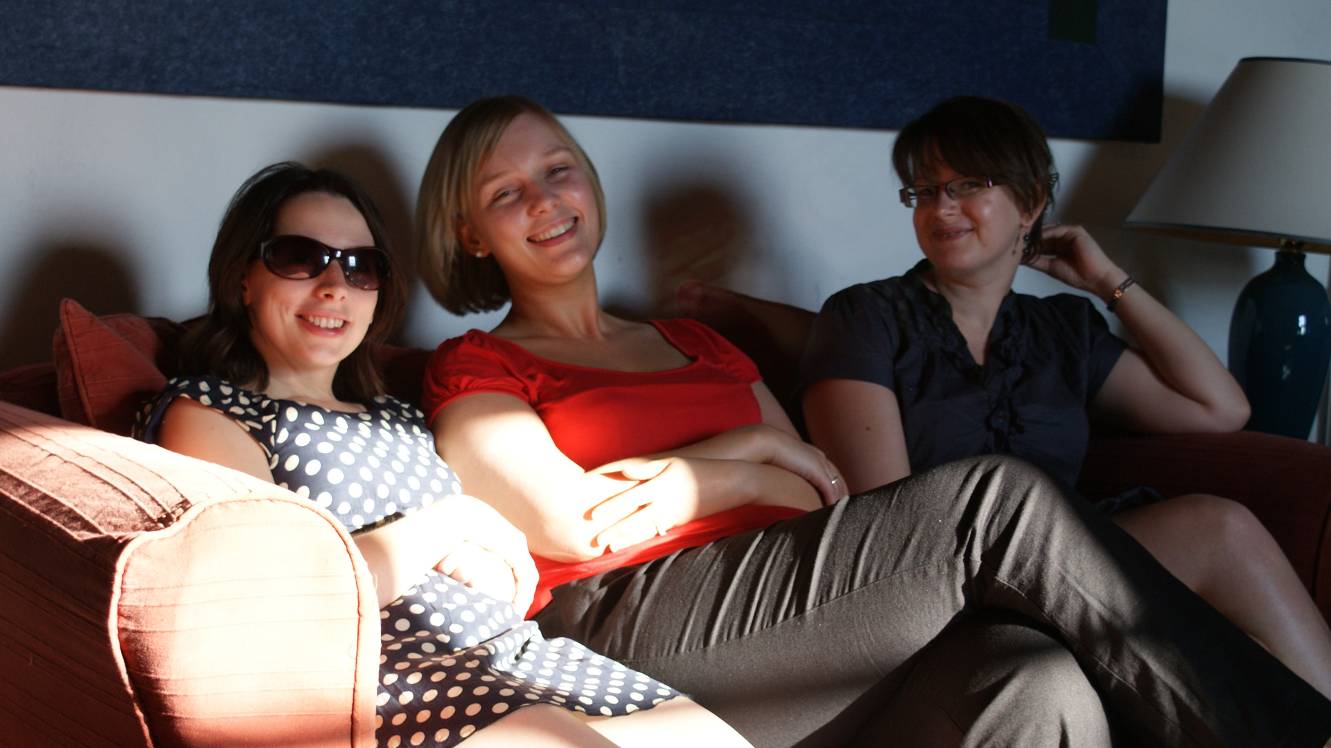 three women sitting together on the couch while one looks off in a camera