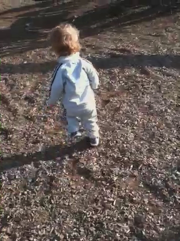 young child in white overalls walking through the woods