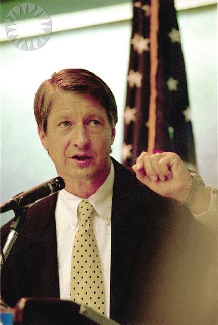 a man in a suit speaking to reporters at a podium