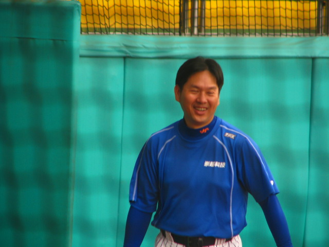 man in baseball uniform standing on a fence smiling