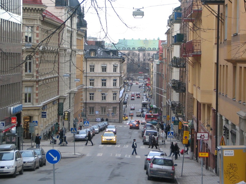 there is a long street with cars parked and pedestrians crossing