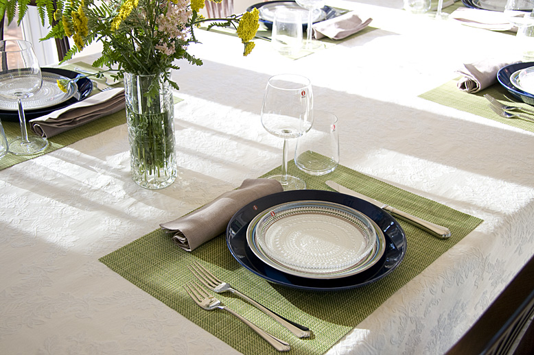 a clean table set for dinner with empty plates and a vase of flowers