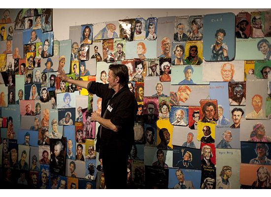 a person points to a wall that is covered in many portraits