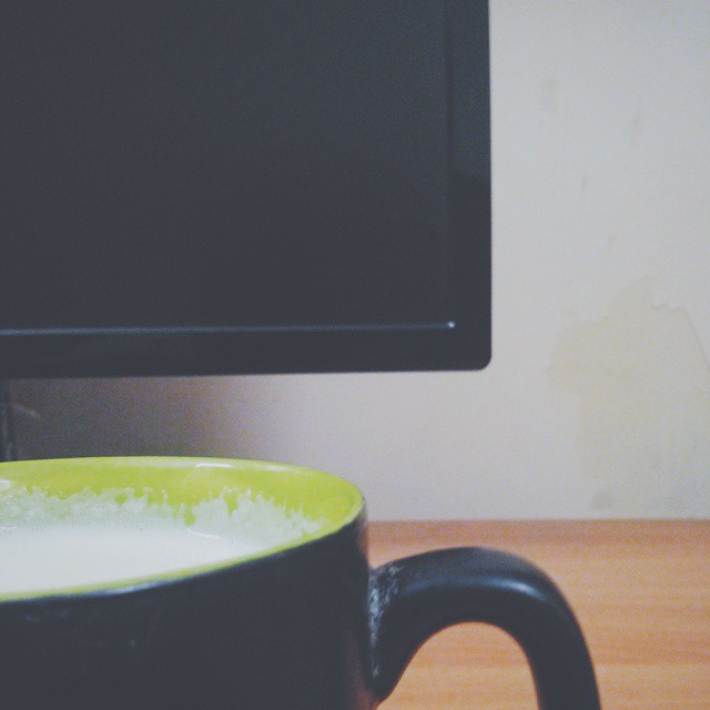 a black and green mug on a table with a monitor