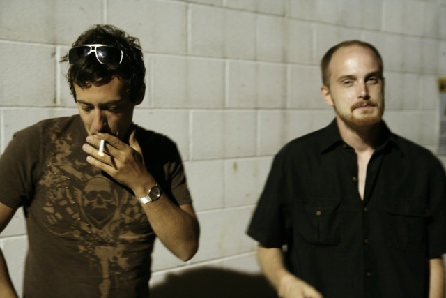 the two men are standing next to each other smoking cigarettes
