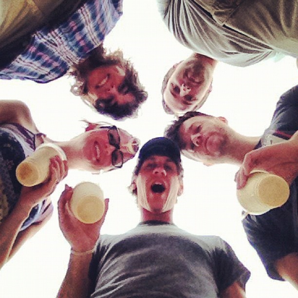 five men standing around holding beers and smiling