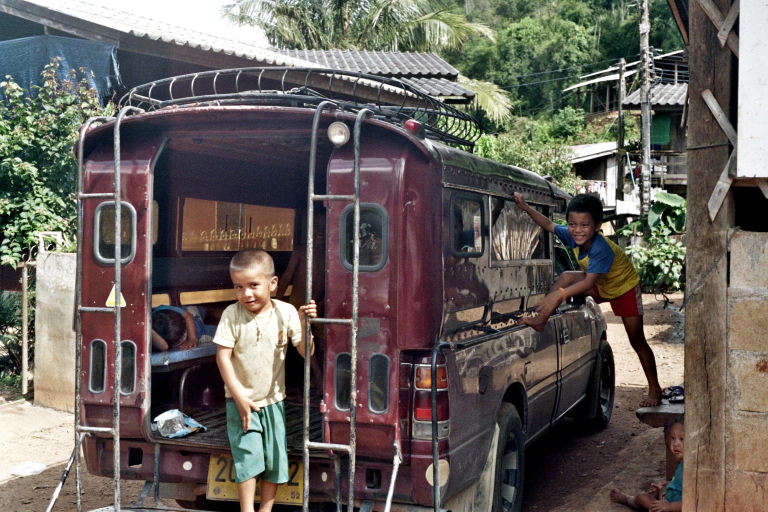 two boys standing outside of a maroon van with open doors