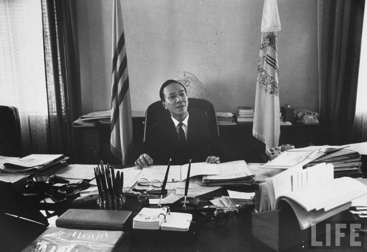 a man in suit sitting at his desk with many papers