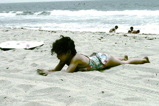 a girl laying on her stomach in the sand