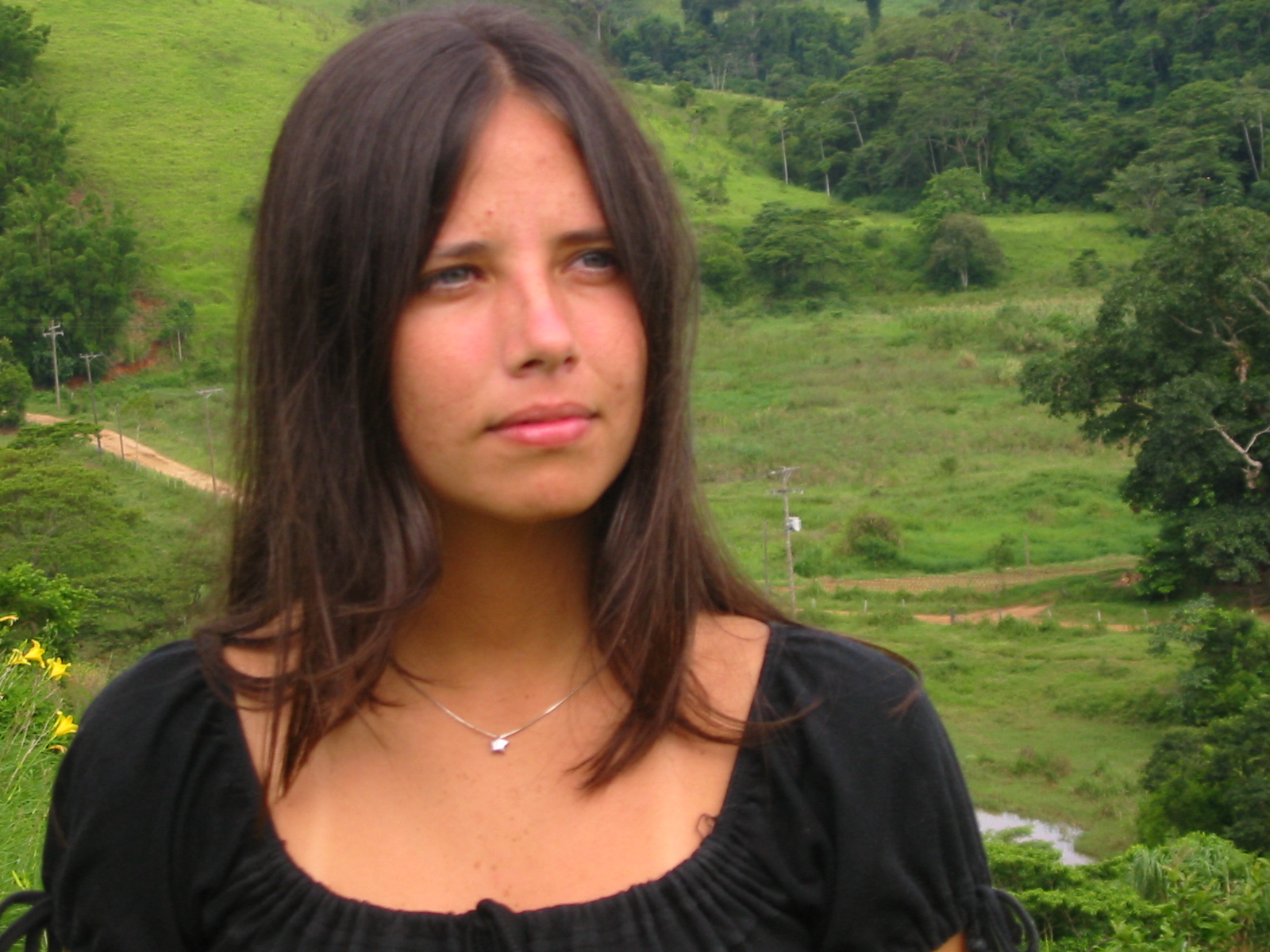 a woman posing in front of a lush green hillside