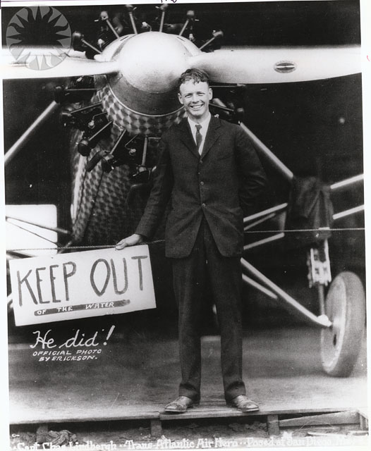 a man in a suit posing with a sign beside a plane