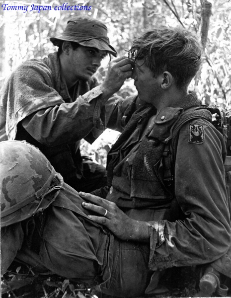 two soldiers sitting in the woods and one is combing the ear