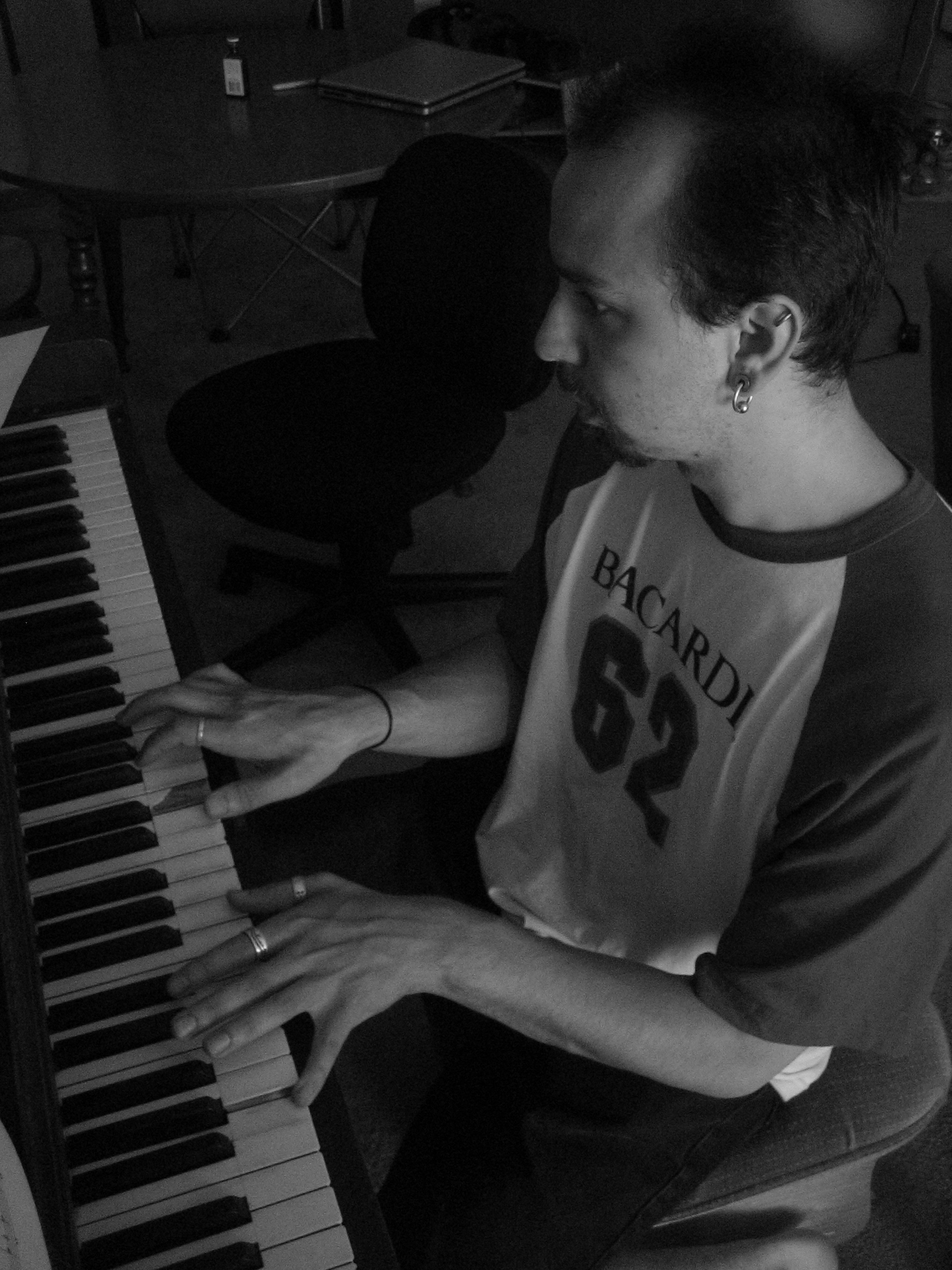 man with ear piercings sitting at a piano keyboard