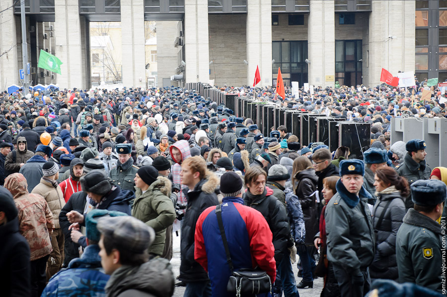 a large crowd of people gathered near a building with doors open