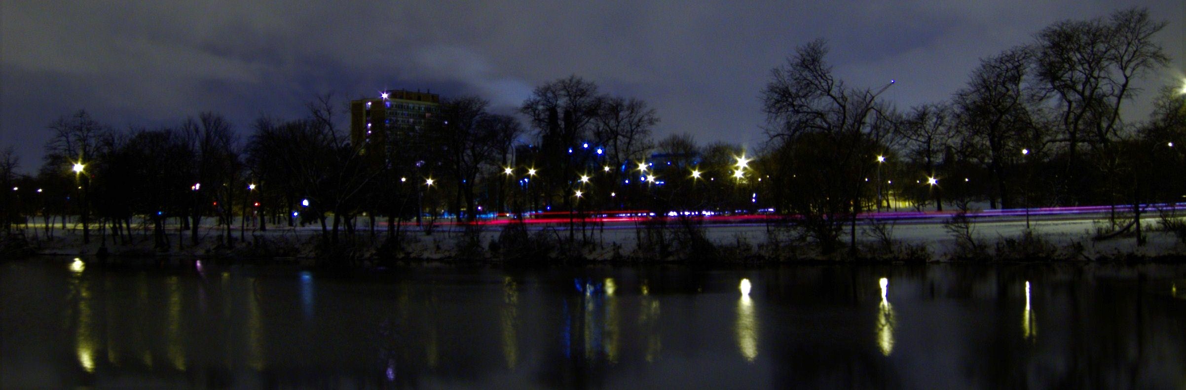 city buildings reflect in the water and trees, with lights reflected in them