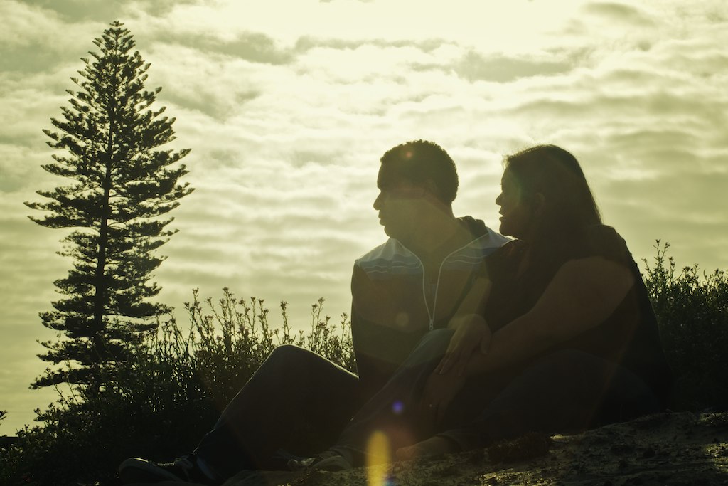 a man and woman sit together as the sun goes down