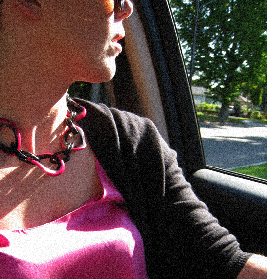 a woman sitting in a car with a pink shirt and necklace