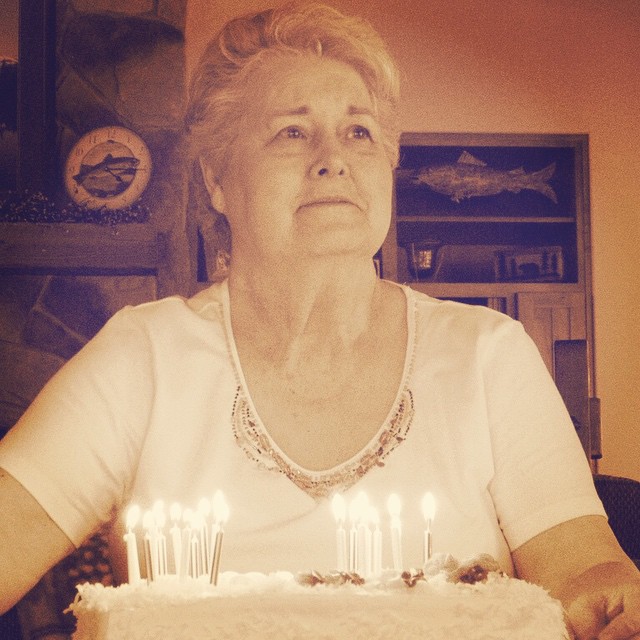 an old woman sitting in front of a cake with lit candles