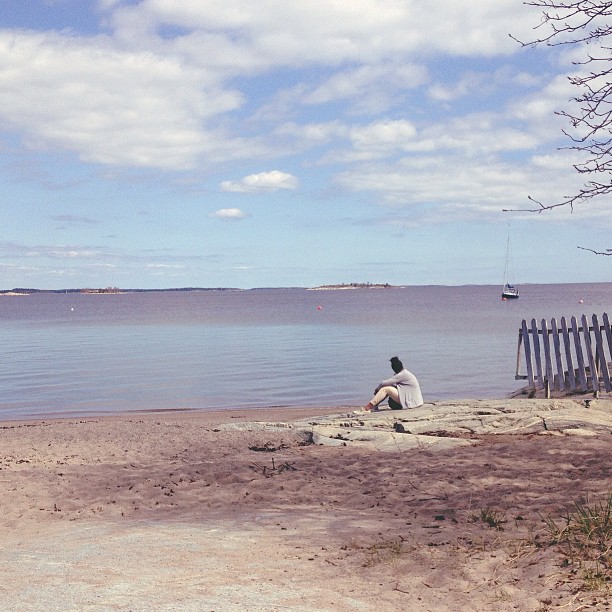 a man sitting on the edge of the beach looking out to sea