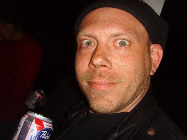 a man with a black hat and glasses looks at the camera while holding a soda in his hand