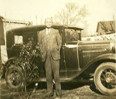 an old black and white po of a man standing next to an antique car