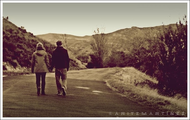 a man and woman walking down the road holding hands