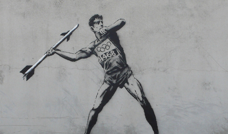 a street painting of a man holding a spear with the olympic sign behind him