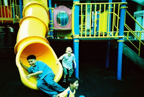 children slide around a playground, two children watch
