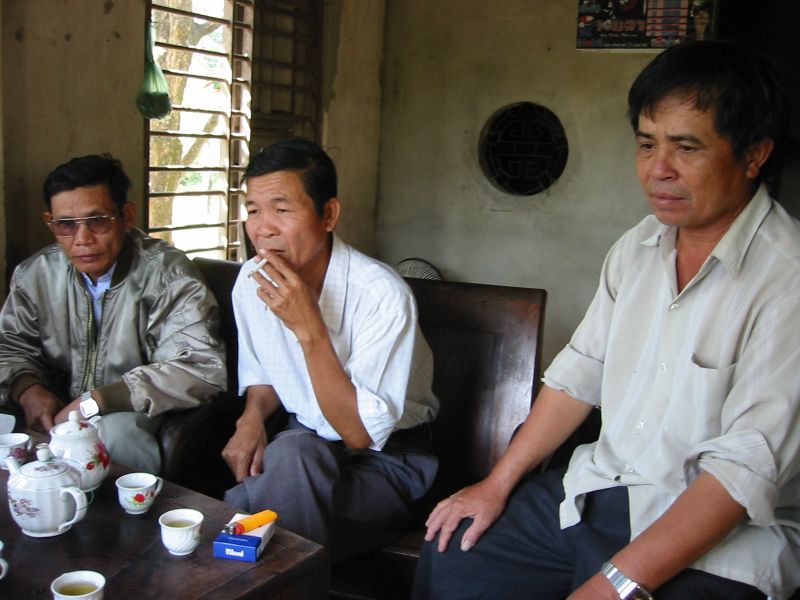 four men sitting together drinking and smoking cigarettes