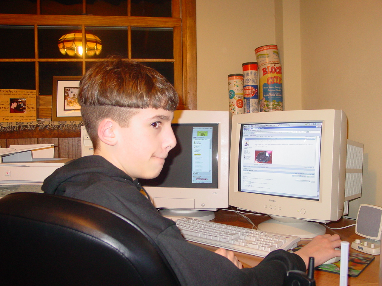 a young man sitting at a computer desk in front of a screen with his head turned towards a monitor