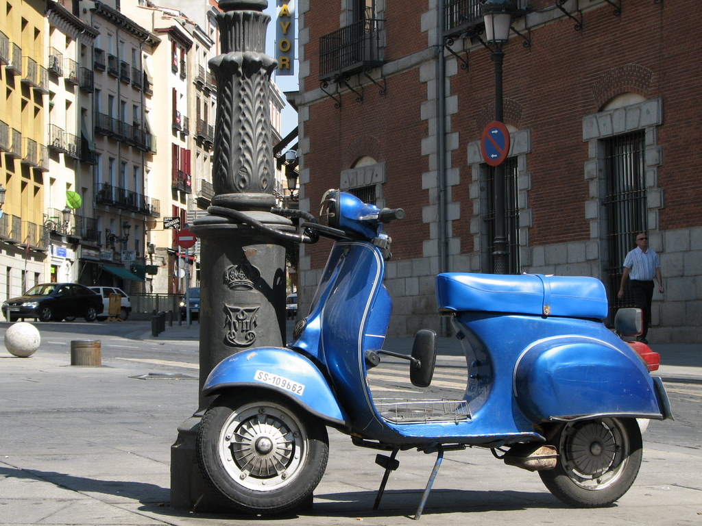 blue motor scooter parked on the side of a city street