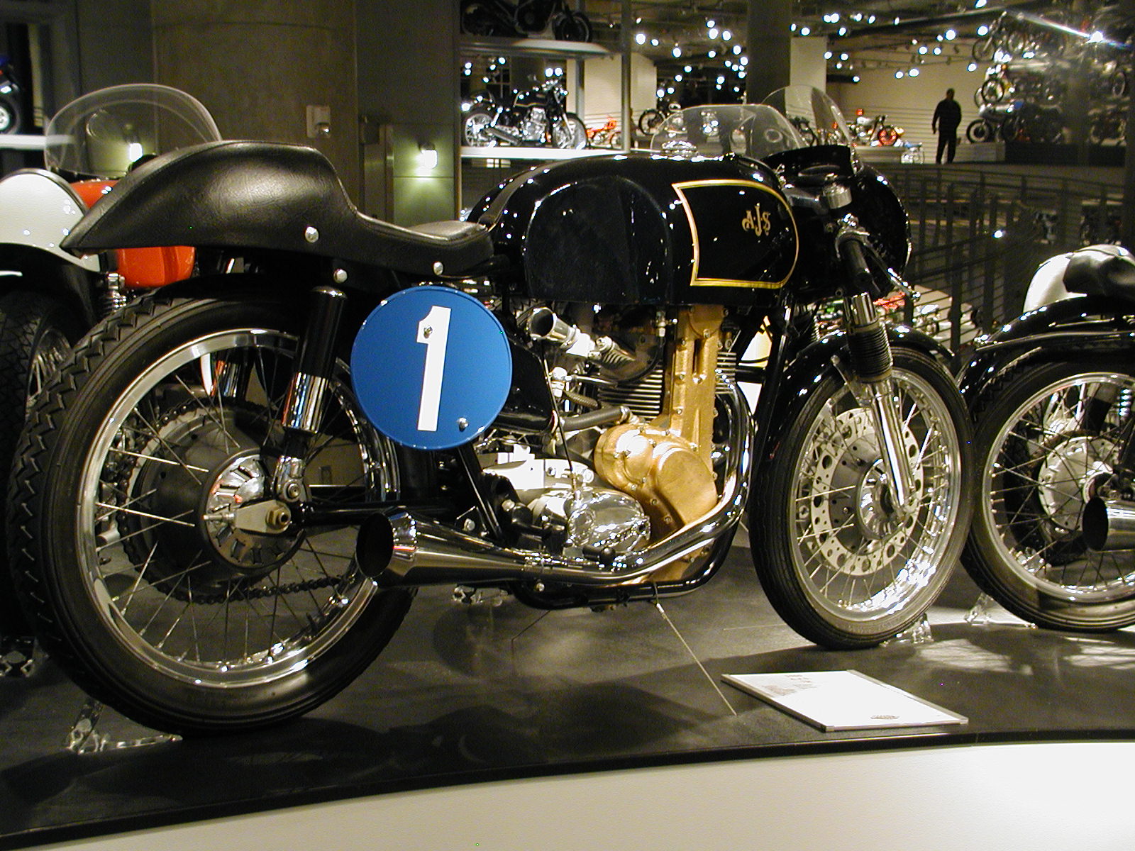 two old fashioned motorcycle on display with people standing