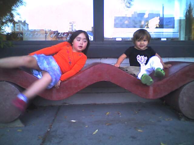 two children are sitting on a bench on the pavement