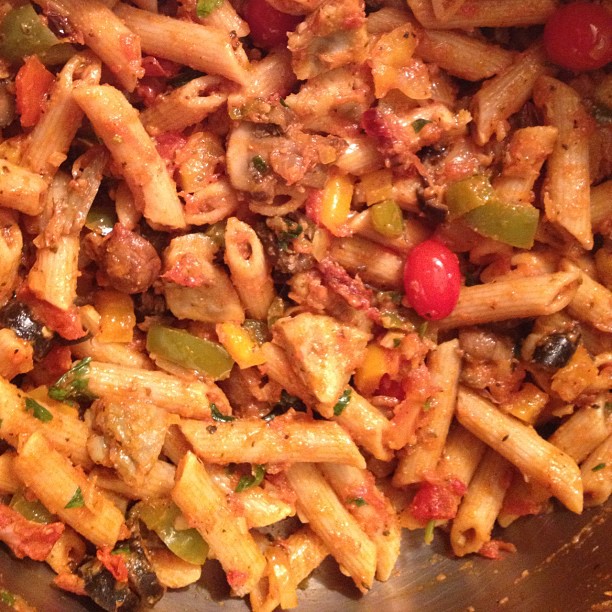 a bowl of pasta with tomatoes, peppers and meat