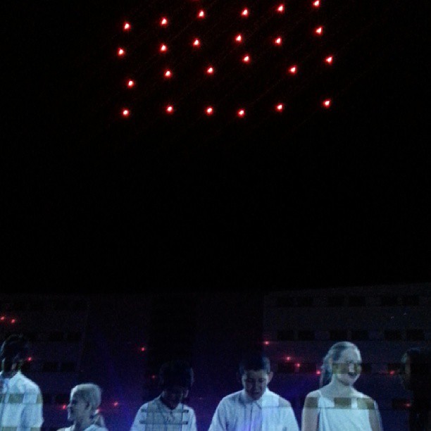 group of people on stage with fireworks in the sky