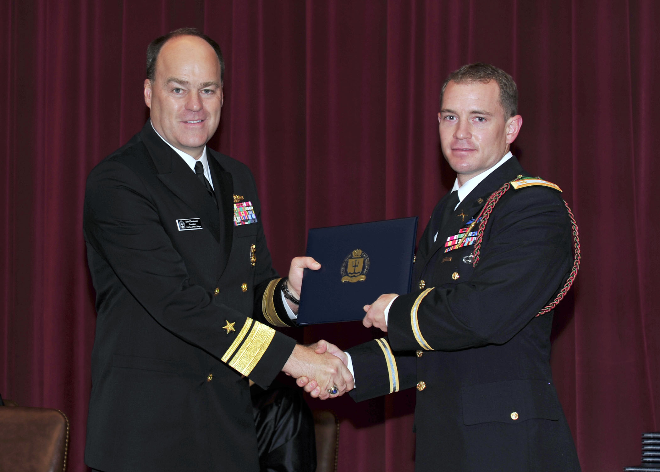 two men in military dress uniforms hold an award