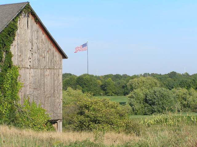 an old red barn with a flag in the distance