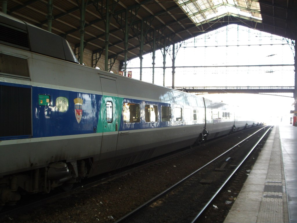 a white and blue train passing under a large roof