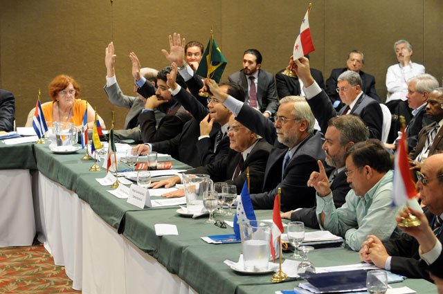 a group of people sit in a conference room with their hands up